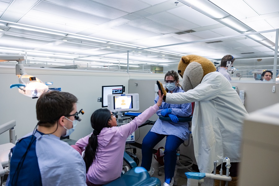 Image of the Goldy the Gopher mascot high fiving a child, surrounded by dentists in a clinic.