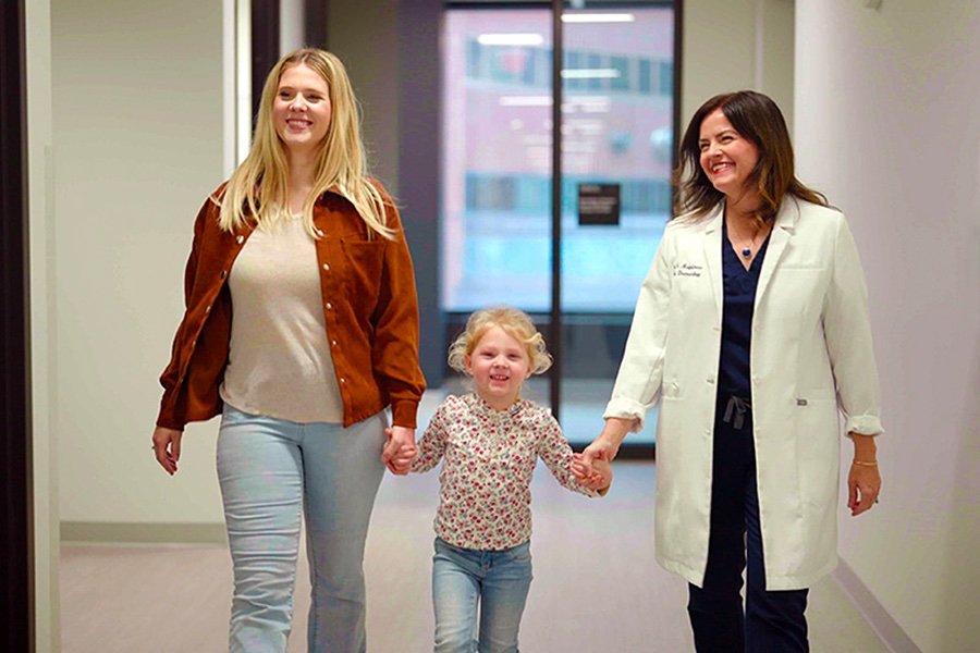 Little blonde Piper Cramer walks between her tall blonde mother and less tall, dark-haired, white-coated Dr. Sheilagh Maguiness.