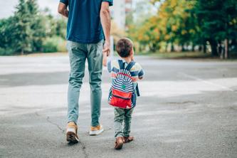 Parent holds hand of little boy with a backpack 