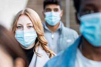 Three people wearing medical masks on a street approach the camera.
