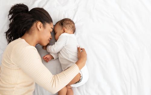 a Black mother with her arm around her sleeping newborn