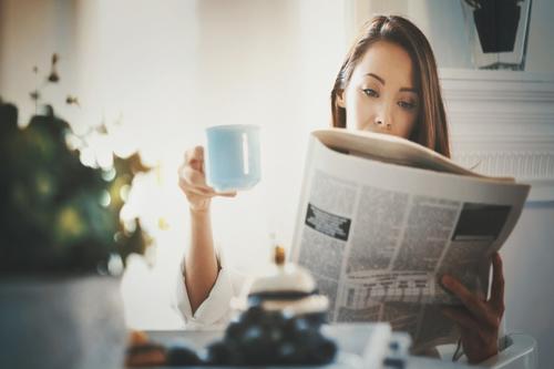Woman drinking coffee and reading newspaper