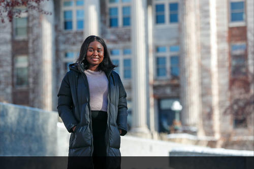 Gbemi Oyetunde wearing long winter coat with columned building in background