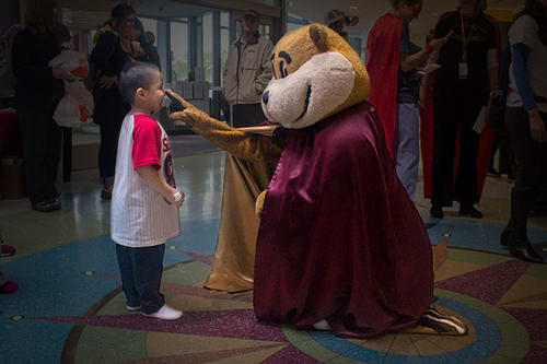 Goldy wearing a cape playing with a boy
