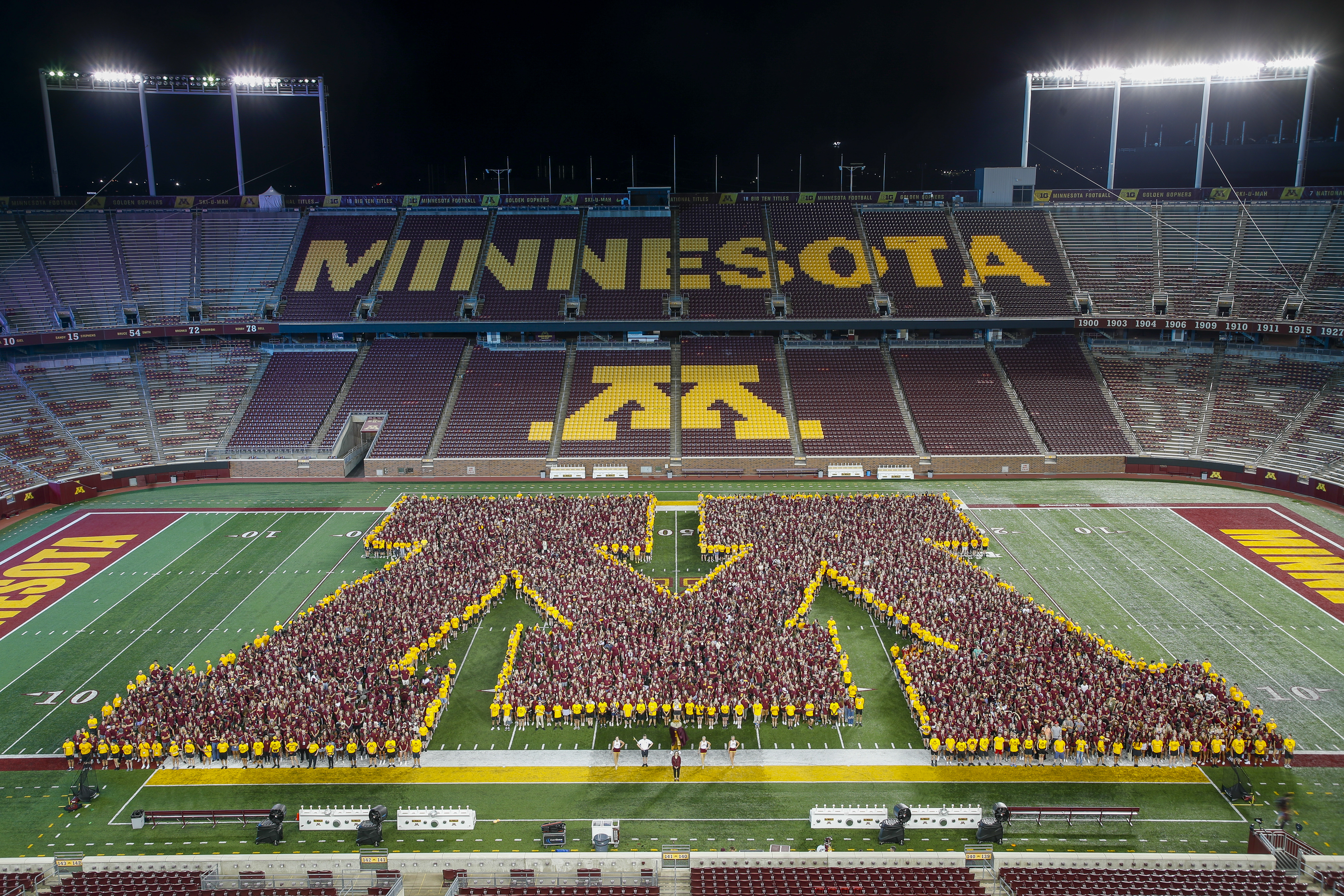 An aerial shot shows approximately 6,700 first year students standing together on the Huntington Bank Stadium football field, forming the Block M logo that represents the U of M