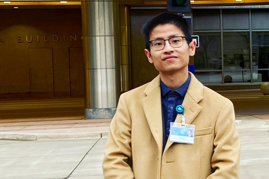 Quincy Gu, in tan blazer, stand in front of a nondescript building.