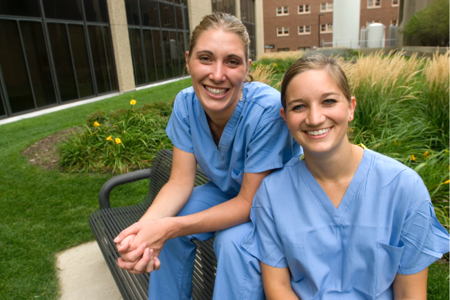 Medical school students posing in their light blue scrubs in grassy plaza