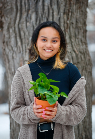 Anna Aquino holds a plant in a pot outside by a tree
