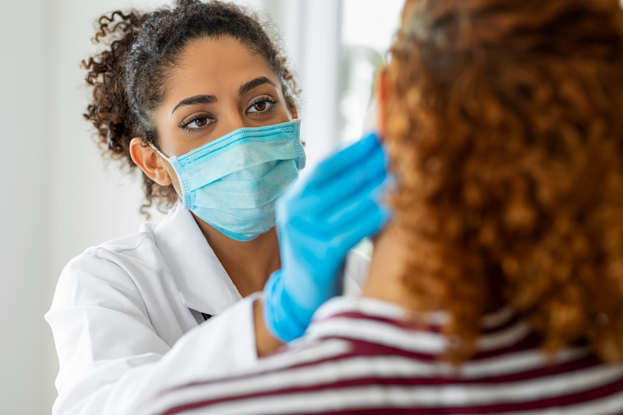 Image of dentist in blue mask and blue gloves examining a patient’s jaw.