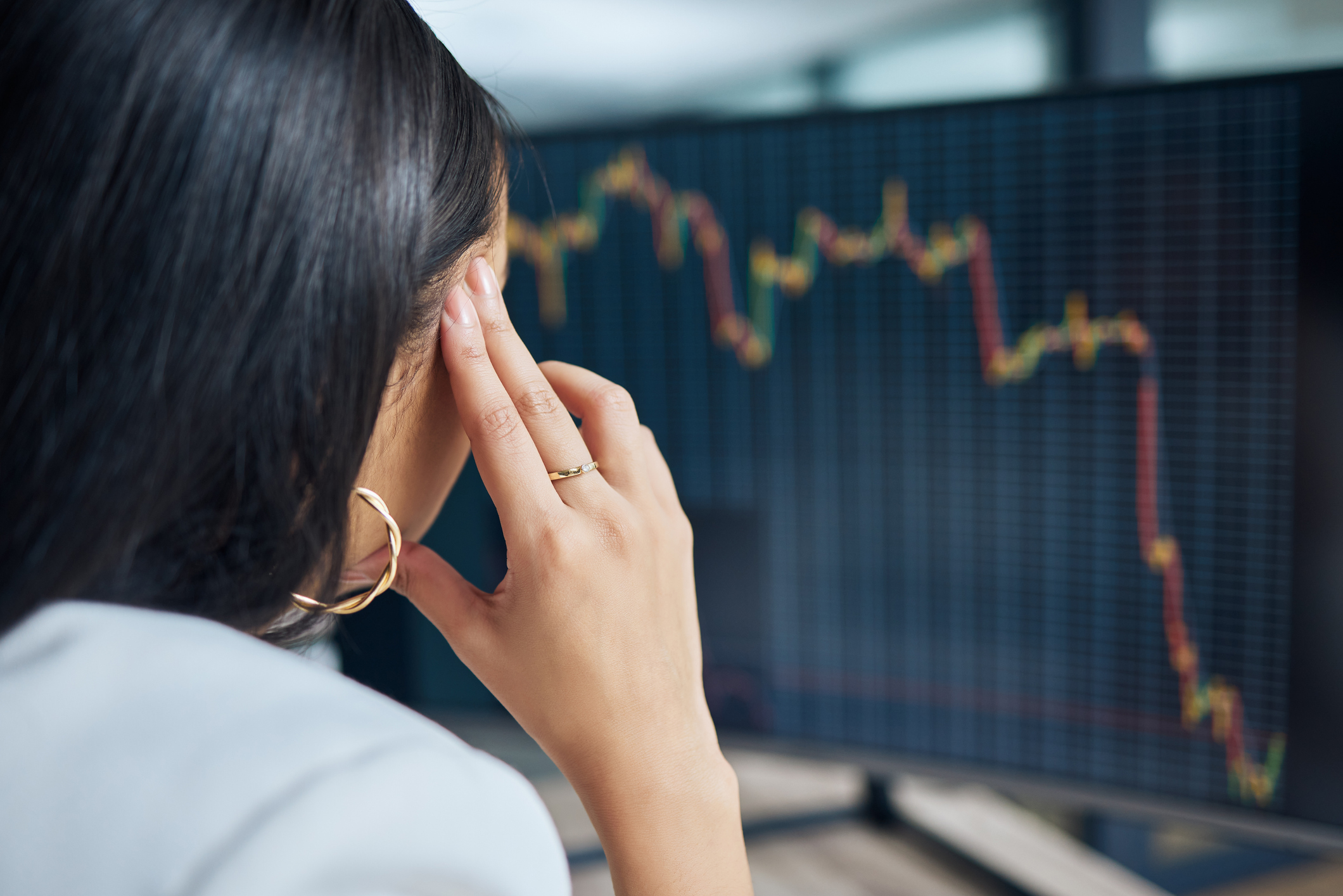 A stressed woman observes declining stock performance on a computer.