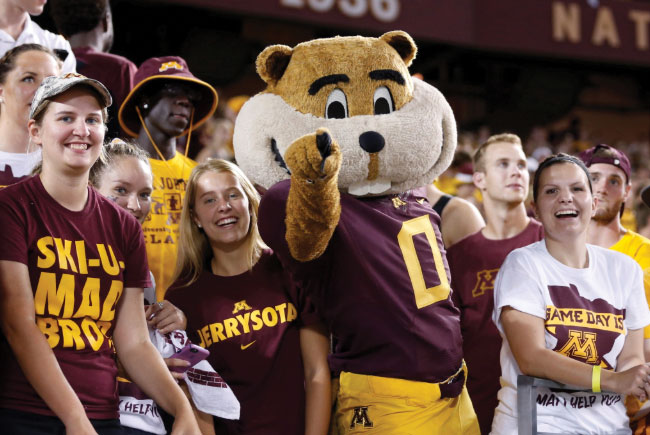 Goldy wearing football uniform posing with fans at game