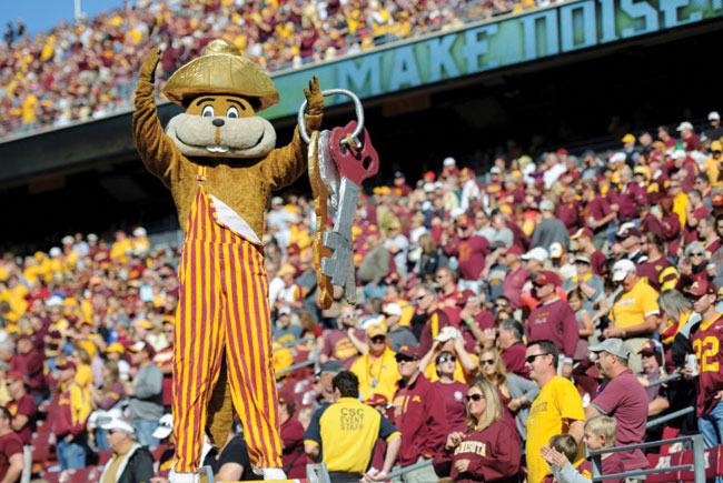 Goldy wearing striped overalls holding oversized keys at football game