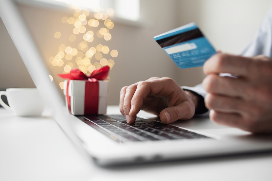Hands hold a credit card and use a computer with a holiday gift in the background.