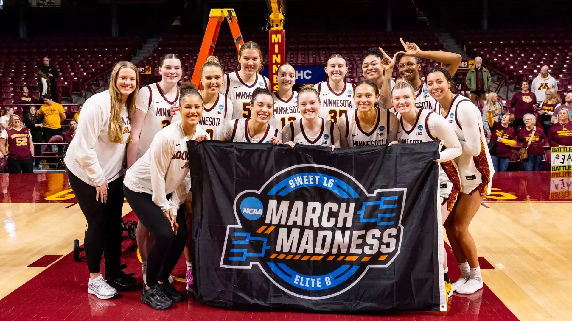 University of Minnesota Gopher women's basketball team standing on a basketball court holding a March Madness banner