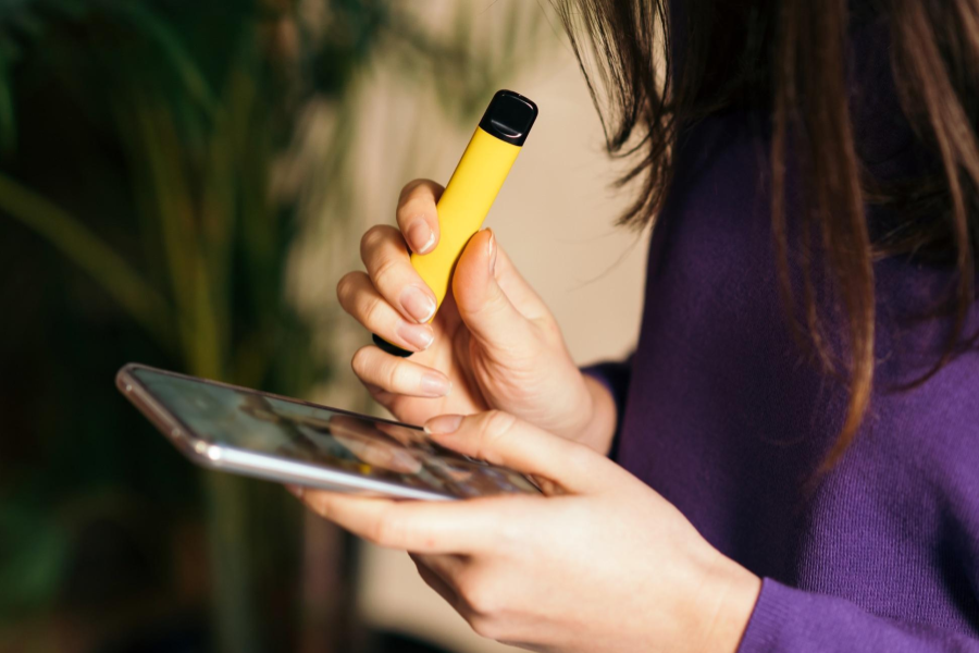 Woman holding a vaping pen and an Apple smartphone