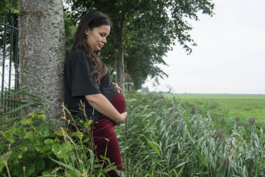 Pregnant woman cradling stomach leaning against a tree