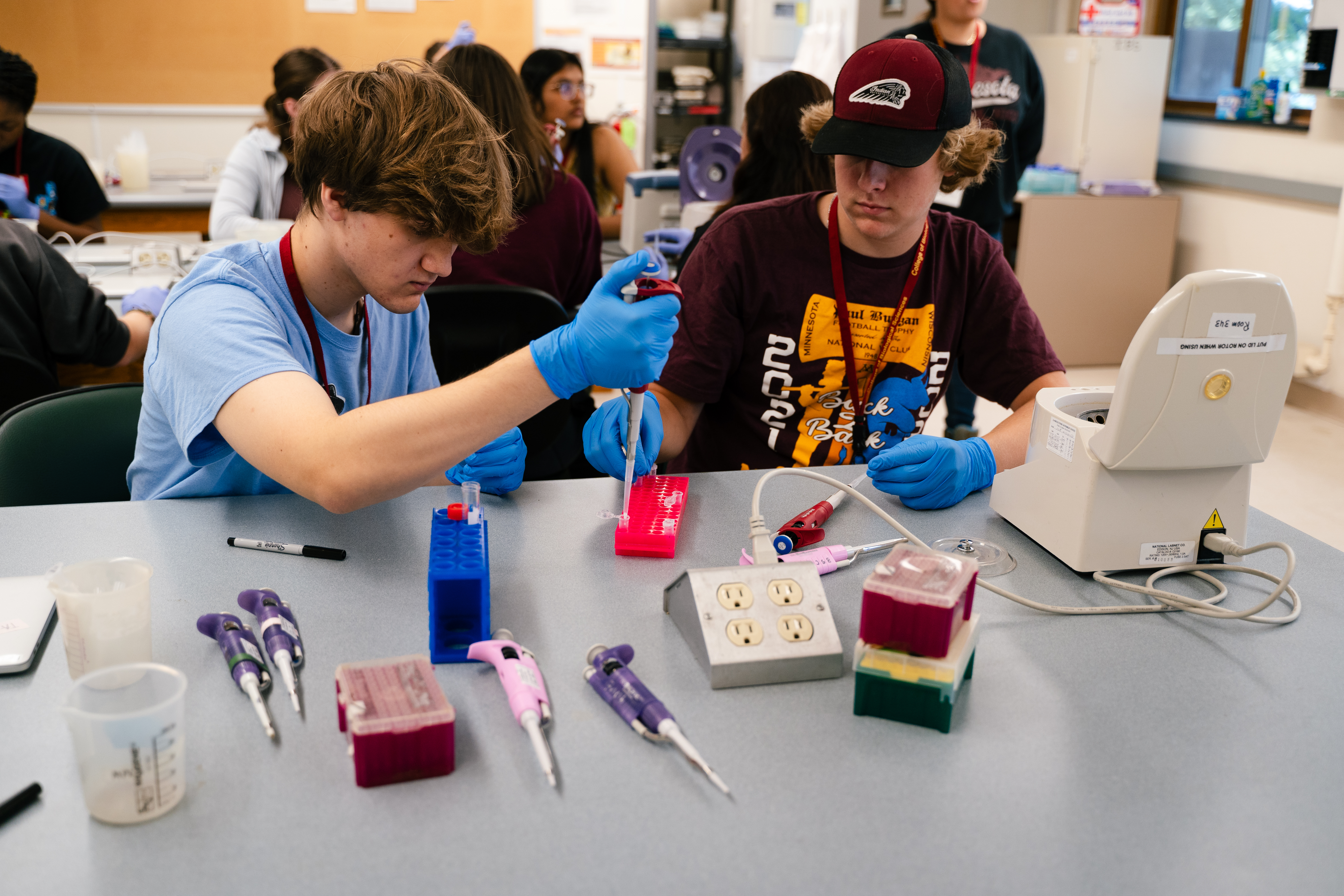 Students, one holding a pipette, work with a bench-top centrifuge.