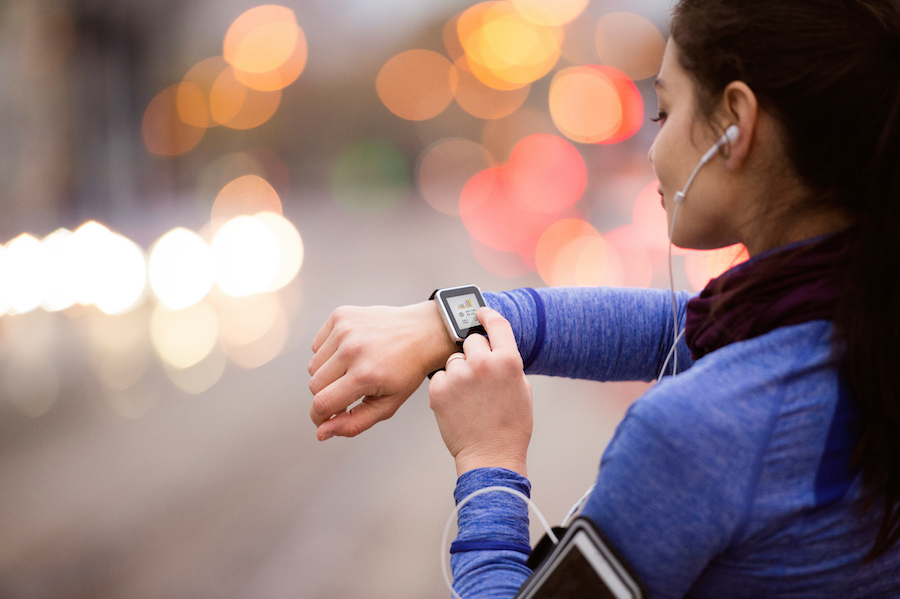 A woman checks her smartwatch with blurry city lights in the background