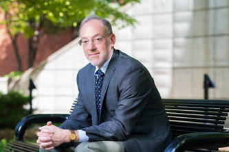 Portrait of Professor Joel Waldfogel seated on a bench outdoors.