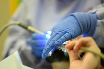 Image of a person’s hand in a blue surgical glove accepting a dental tool from another person.