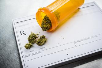 Image of an orange prescription bottle lying on top of a prescription paper pad that says “Rx” on it. There are nuggets of marijuana coming out of the bottle onto the prescription pad