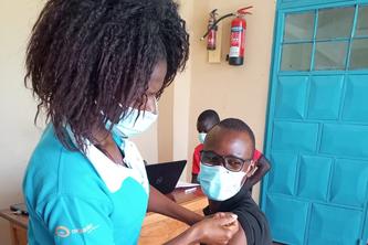 Image of a woman wearing a mask administering a vaccine to a man sitting down with a mask.