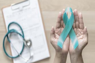 Image of hands holding a teal ribbon - which symbolizes ovarian cancer - next to a clipboard with a stethoscope on top of it.