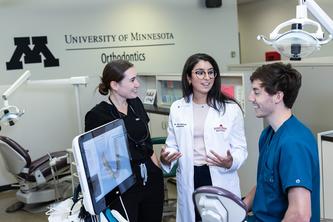 Image of Dr. Petra Bachour talking to two dentistry students in scrubs in front of a monitor that shows an x-ray of teeth.