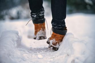 Image of someone’s pair of boots walking through the snow, one ankle slightly bent as if they are about to stumble.