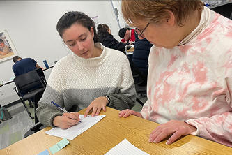 Isabelle Morris writes on a sheet of paper while another person looks on.