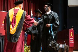 Corey Dawson receives diploma on stage with Oscar the dog at side.