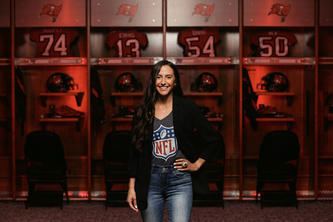 Emily Lekahal stands in front of football jerseys and helmets in a display case