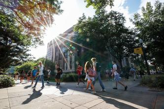 Dozens of students walking across a busy campus pedestrian area