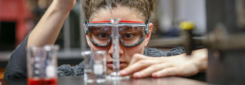 A female student wearing safety goggles and concentrating while dropping chemicals into a vial
