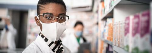 Black female student wearing glasses and white face mask and white lab coat