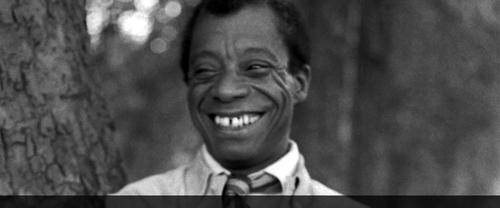 James Baldwin smiling and leaning on tree