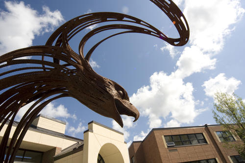 A bronze-colored eagle sculpture overlooks the entrances to buildings on the U of M Crookston campus on a sunny afternoon