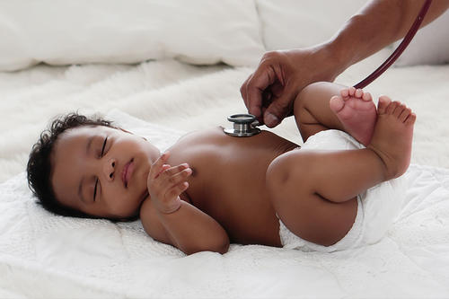 A health care worker uses a stethoscope on a Black baby.