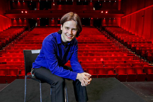 Colin Covert sits in chair on stage with theater seats visible in background