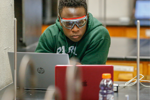 Student wearing goggles monitors experiment data in two different laptops on table