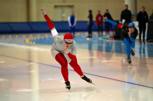 Ilsa Shobe, in red cap, dark goggles and red leggings, skates hard on a track.