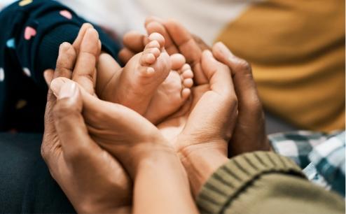 Black adult hands cradling the feet of a small Black child