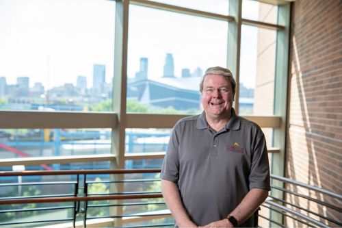 Portrait of Mark Bergen infront of a window overlooking downtown Minneapolis