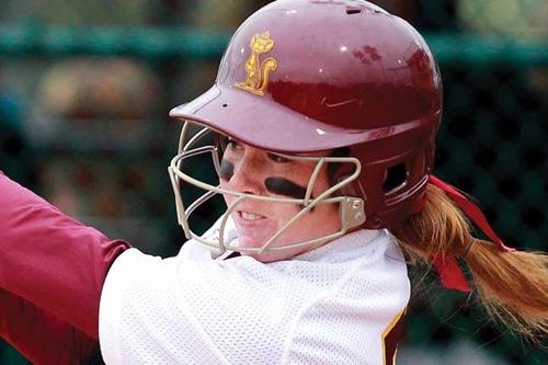 Woman playing softball is seen in a close up picture through her wire facemask, attached to her Maroon batting helmet with a Gold, throwback version of Goldy Gopher on it