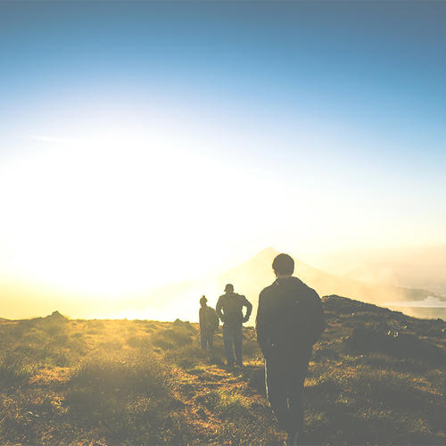Three people walk on mountain path in sunset