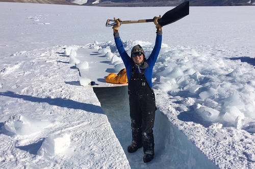 Heidi Roop stands inside a share-edged snow trench holding a square-ended shovel aloft. 