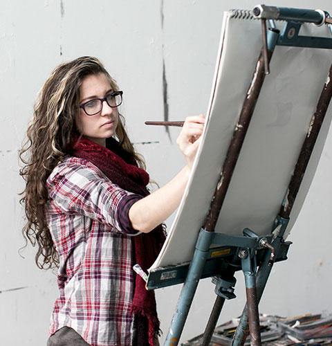 A female student painting on a canvas being held by an easel