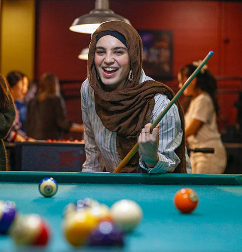 A student smiling in reaction to a pool game holding a pool cue