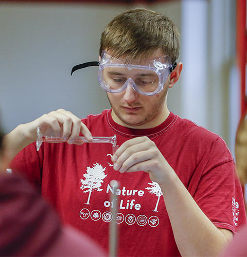 A male student pouring into a beaker wearing safety glasses