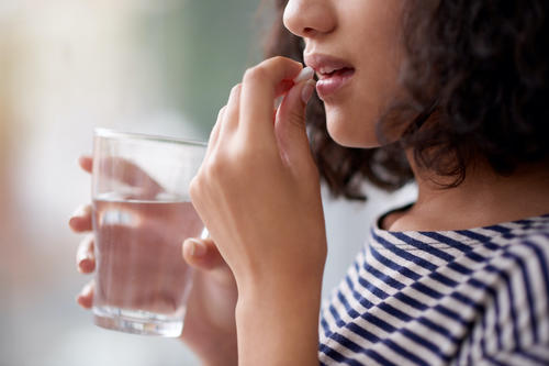 A woman putting a diet pill in her mouth while holding a glass of water